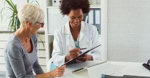 A female doctor sits at her desk and chats to an elderly female; blog: do women see urologists