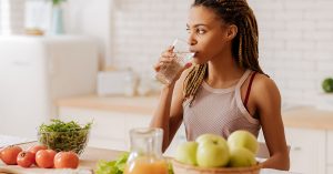 Water before breakfast. Slim and fit woman with many little braids drinking water before having breakfast; blog: Changing Your Diet to Prevent Kidney Stones