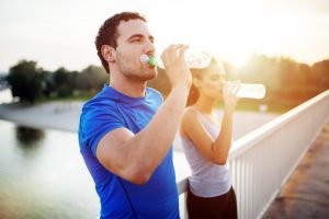 a man and a woman in athletic apparel drinking water bottles and staying hydrated